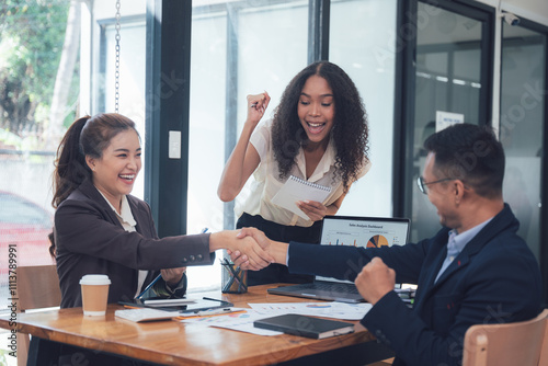 Business Deal Sealed: A jubilant moment in a modern office setting, as a diverse group of professionals celebrates a successful deal with a firm handshake and beaming smiles.