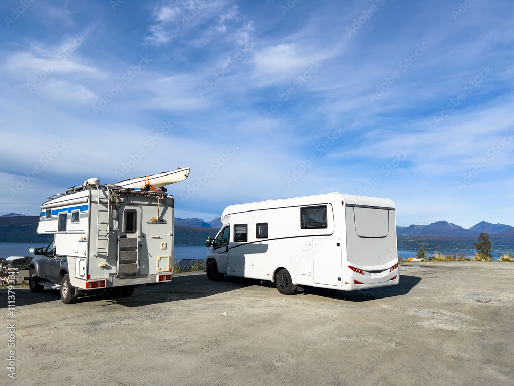 Naklejka premium Two camper vans are parked near a scenic lake and mountain range, embodying the spirit of travel and adventure