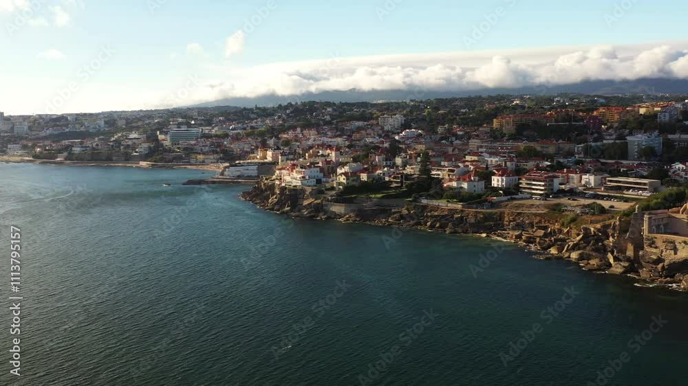 Panoramic aerial view of Estoril, Portugal, shot from the ocean. In the distance, the Sintra mountain can be seen against an overcast sky, creating a stunning contrast with the coastal town cinematic Panoramic aerial view of Estoril, Portugal, shot from the ocean. In the distance, the Sintra mountain can be seen against an overcast sky, creating a stunning contrast with the coastal town cinematic