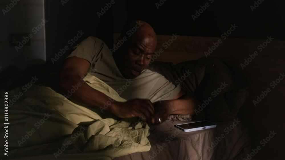 Middle aged Black man sleeping in bed at night, waking up from asthma attack and using inhaler to stop coughing Middle aged Black man sleeping in bed at night, waking up from asthma attack and using inhaler to stop coughing