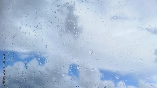 Rain water or dew drops on wet transparent car glass window or windshield surface with cloud blue sky background. Rainy season, condensation, spring, storm, rainfall, cloudscape and typhoon concept.