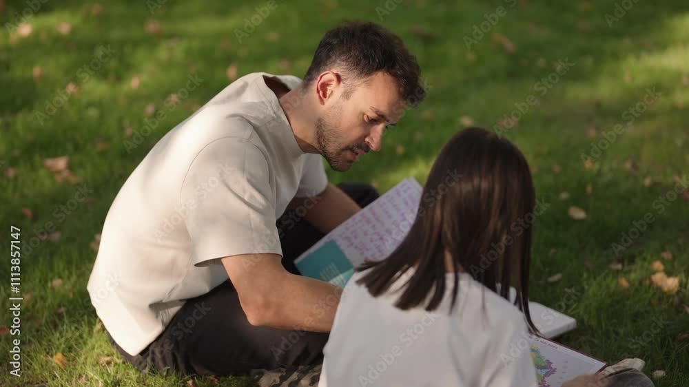 Caring father assisting his young daughter with her schoolwork in a serene outdoor setting, fostering a love for learning.