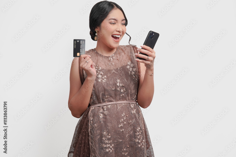 Happy young Asian woman wearing brown brocade dress holding a credit card and a cell phone. Happy young Asian woman wearing brown brocade dress holding a credit card and a cell phone.