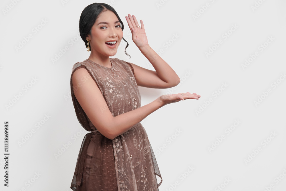Smiling Asian woman wearing brown brocade dress pointing to the copy space beside her. Smiling Asian woman wearing brown brocade dress pointing to the copy space beside her.