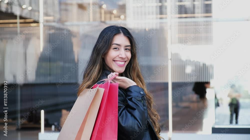 Young woman is holding shopping bags and smiling outside a department store Young woman is holding shopping bags and smiling outside a department store