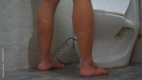 Man is peeing into the toilet bowl. Low angle view of a man feet entering the toilet. A man is urinating in the toilet