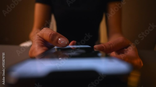 High-angle view of woman using smartphone in dark room, scrolling through social media or browsing online content. Top view of female using mobile phone in dimly lit room. Shooting in slow motion.
