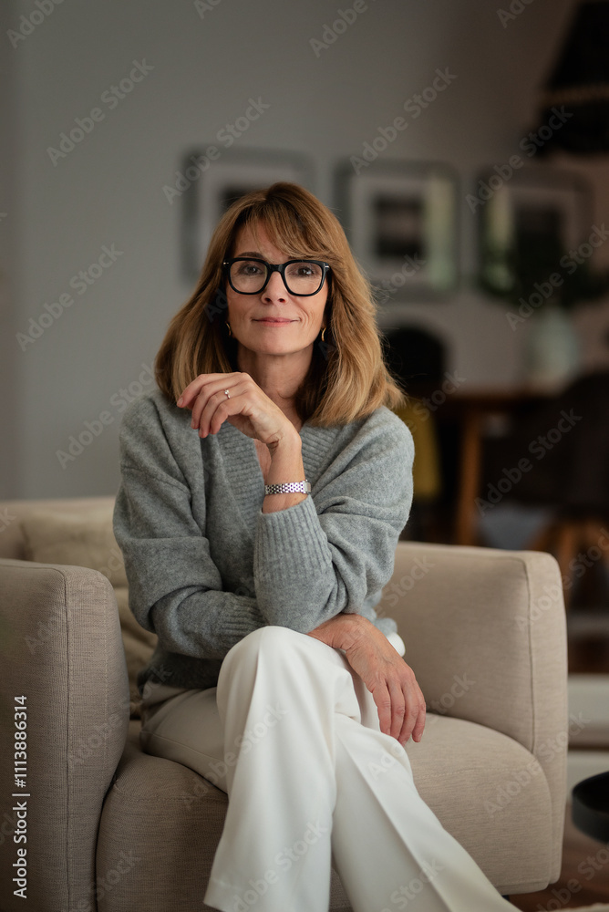 Smiling woman sitting in an amrchair in her cozy home and smiling at camera Smiling woman sitting in an amrchair in her cozy home and smiling at camera