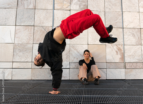 A man performs a breakdance pose while a girl watches him