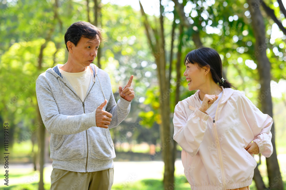 Cheerful father and adult daughter in a lively conversation while exercising together in a park Cheerful father and adult daughter in a lively conversation while exercising together in a park