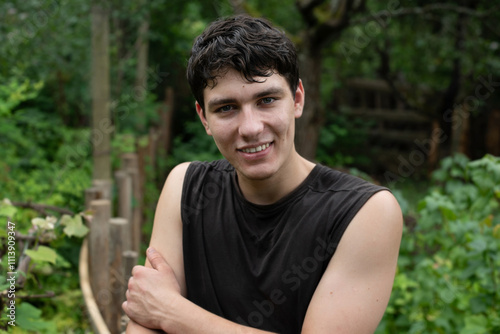 The guy is happy and smiling even though he is tired after running along the forest paths. A young man is captured smiling warmly in vibrant, lush garden, surrounded by greenery