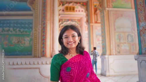 Portrait of beautiful young woman wearing saree and smiling at camera while standing at Patrika Gate, Jaipur, India.  Female tourist posing, Indian culture and traditions. 
