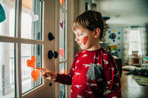 Boy in red dinosaur shirt with glitter heart touches window hearts photo