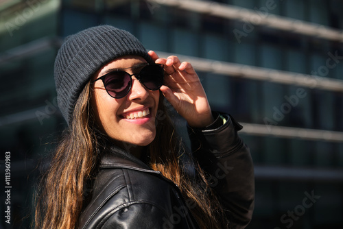 Stylish woman wearing sunglasses and beanie smiling in urban setting