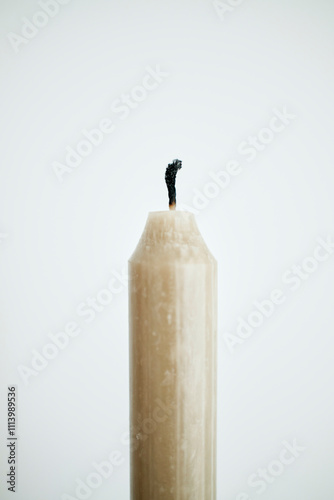 Close-up of an unlit beige candle with a burnt wick against a white background.