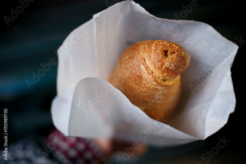 Fresh croissant bread roll in a white paper bag held by a person with a checkered sleeve. photo