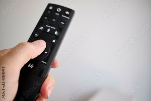 Close-up of a hand holding a black television remote control against a blurred white background. photo