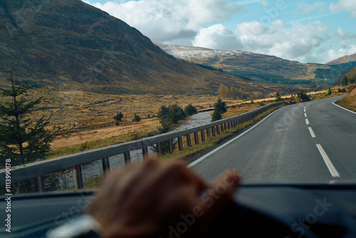 Mountain landscape viewed from a car with the driver's hand on the steering wheel, Highlands, Scotland photo