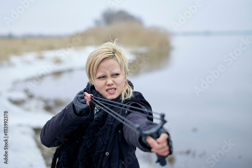 Woman with a determined expression aiming a slingshot in a snowy landscape, East Germany photo