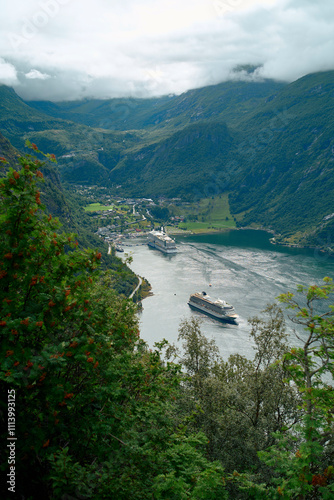 Majestic fjord with a cruise ship docked near a 0uaint village surrounded by lush green mountains under a cloudy sky, Geirangerfjord, Norway photo