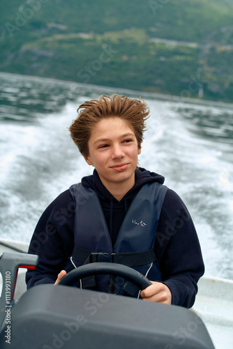 Confident teenager steering a boat with water churned up in the background, Geirangerfjord, Norway photo