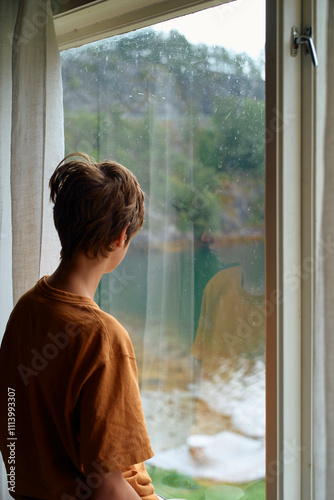 Young boy gazing out of a rain-splattered window on a gloomy day, Geirangerfjord, Norway
