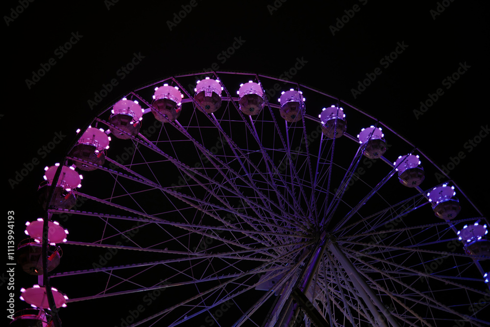 A Ferris wheel illuminated with purple lights against a dark night sky, Poznan, Poland A Ferris wheel illuminated with purple lights against a dark night sky, Poznan, Poland
