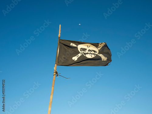 A pirate flag with a skull and crossbones flutters against a clear blue sky with a crescent moon, Fuerteventura, Spain photo