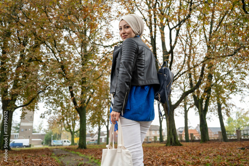 Woman with a headscarf and leather jacket carrying bags in an autumnal park setting, Netherlands photo