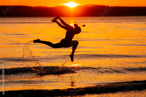 Silhouette of a person performing a ballet pose on a beach at sunset with reflections on the water, USA photo