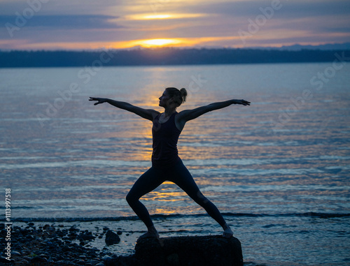 Silhouetted person striking a yoga pose on a rock by the seashore at sunset. photo