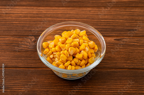 Glass bowl filled with vibrant yellow corn kernels on a rustic wooden background, showcasing a fresh and appetizing close-up of this healthy vegetable
