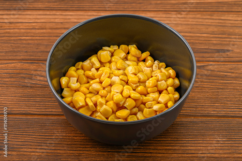 Close-up of vibrant yellow corn kernels in a sleek black clay bowl on a rustic wooden background, creating an appetizing and colorful presentation of this nutritious vegetable