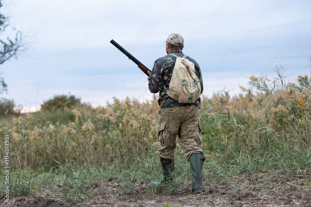 Mature hunter man holding a shotgun and walking through a field Mature hunter man holding a shotgun and walking through a field