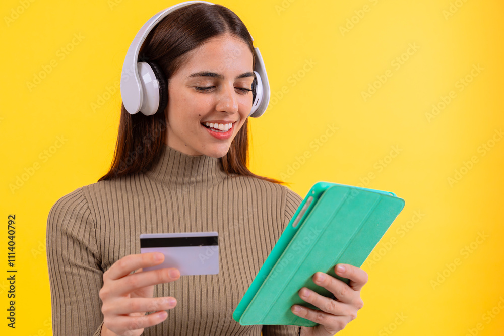 A woman smiles while holding a tablet and a credit card in front of a bright yellow background. His joyful expression creates a positive and engaging atmosphere. A woman smiles while holding a tablet and a credit card in front of a bright yellow background. His joyful expression creates a positive and engaging atmosphere.