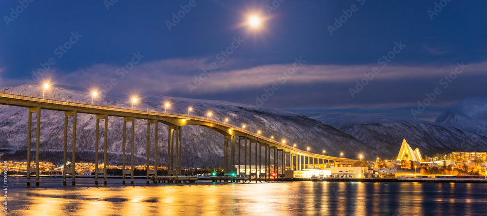 Naklejka premium Panorama of the Norwegian city of Tromso on a winter evening during the Christmas season. The bridge over the fjord and houses are illuminated by city lights