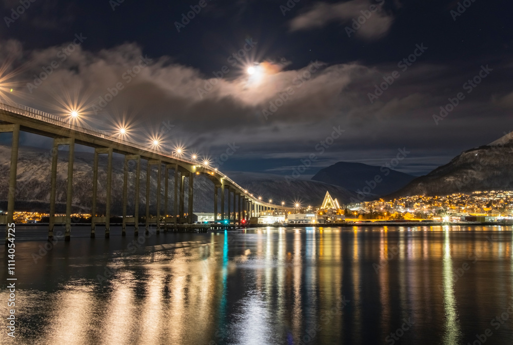 Panorama of the Norwegian city of Tromso on a winter evening during the Christmas season. The bridge over the fjord and houses are illuminated by city lights Panorama of the Norwegian city of Tromso on a winter evening during the Christmas season. The bridge over the fjord and houses are illuminated by city lights