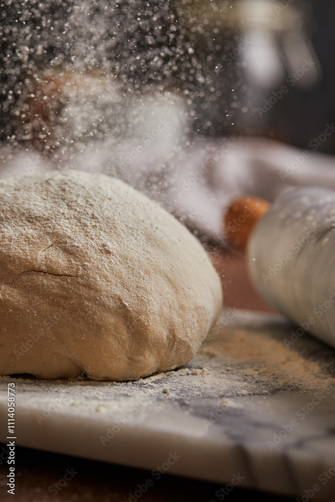 Cooking homemade bread. Sieving flour over raw bread dough rolled with rolling pin on marble board, dark background, selective focus. Baker hands on dough. Cooking homemade bread. Sieving flour over raw bread dough rolled with rolling pin on marble board, dark background, selective focus. Baker hands on dough.