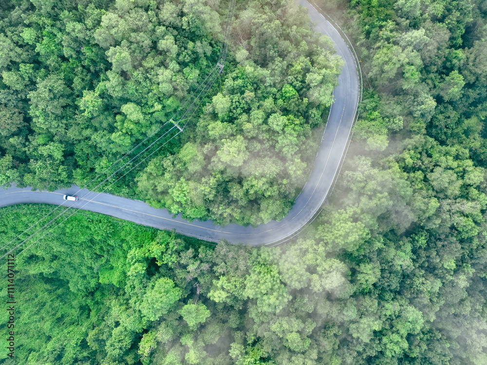 Aerial top view of electric vehicle driving on a winding highway road in green forest with fog. Sustainable transportation, zero emissions, and eco-friendly mobility for reducing carbon footprints. Aerial top view of electric vehicle driving on a winding highway road in green forest with fog. Sustainable transportation, zero emissions, and eco-friendly mobility for reducing carbon footprints.