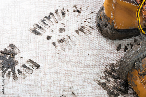 A close up of the wet muddy footprints on the carpet or floor in the living room. A pair of brown boots on the background. Concept of cleaning and dirty stains photo