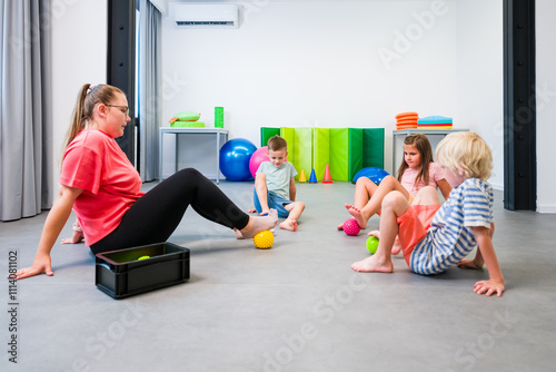 Children and physical therapist during physical therapy session. Kids exercising barefoot with textured surface ball in physio therapy.