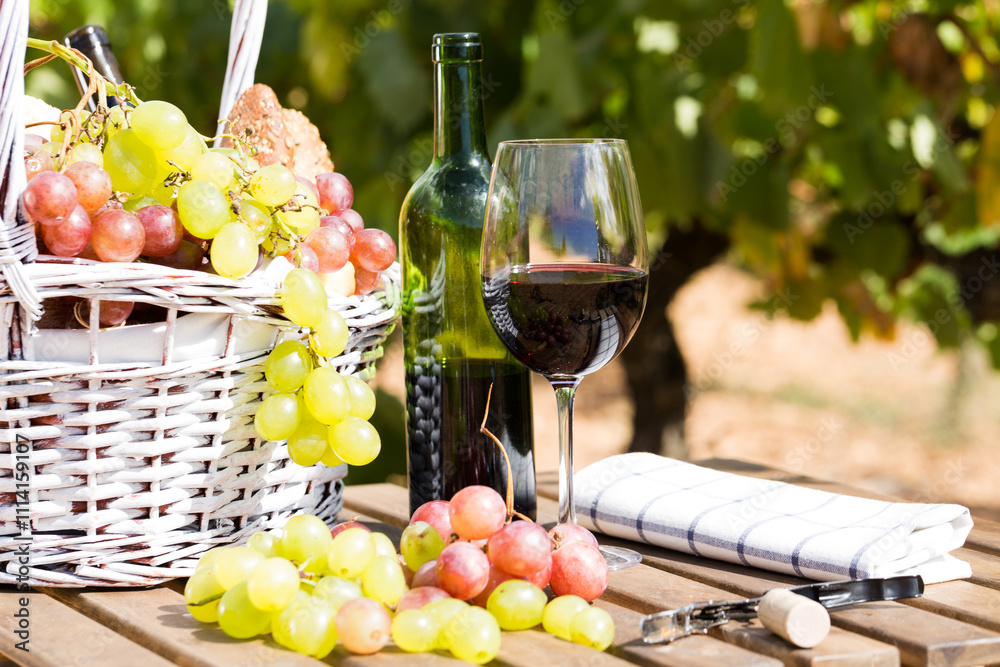 Still life with glass of red wine grapes and picnic basket on table Still life with glass of red wine grapes and picnic basket on table