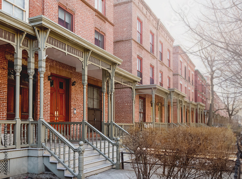 Row of brick buildings. The buildings have a classic old-fashioned look. The porch is decorated with wooden railings. Harlem Houses in New York City. House on Astor Row.