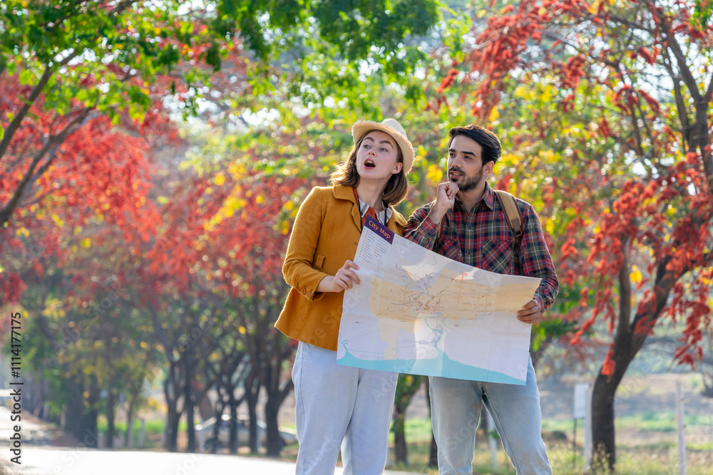 Naklejka premium young caucasian couple traveling in autumn park,they are looking at a paper map for direction