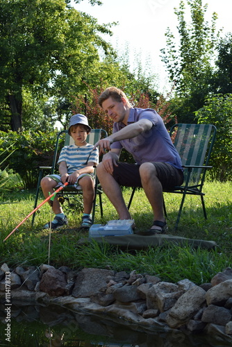 A young father and his son enjoy quality time together, fishing at a pond. The father teaches his son the basics of fishing, creating cherished memories during their outdoor family bonding experience