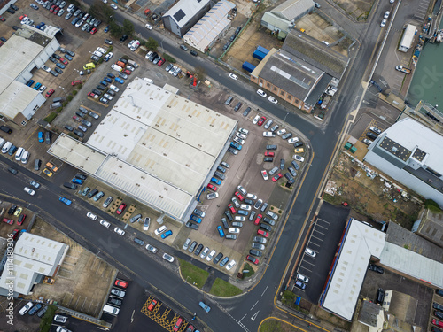 Aerial view of a large, British car dealership seen near a commercial port and dock. Demonstration as well as new and second hand cars are seen on the large forecourt in an industrial area in Suffolk.