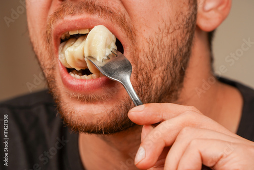A detailed shot of a dumpling on a fork near an open mouth, focusing on the textures of the food and human interaction. Three dumplings in a man's mouth. Perfect for food themes.