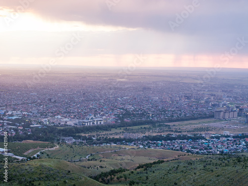 Drone view of the town and mountains at sunset. Haze covered the city. Blue and pink clouds on the sky. Evening landscape.