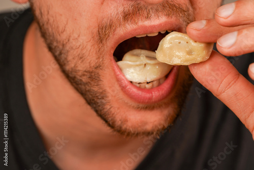 A man puts a vareniki into his mouth, demonstrating the joy of delicious home cooking. A man eats pelmeni with his hands.