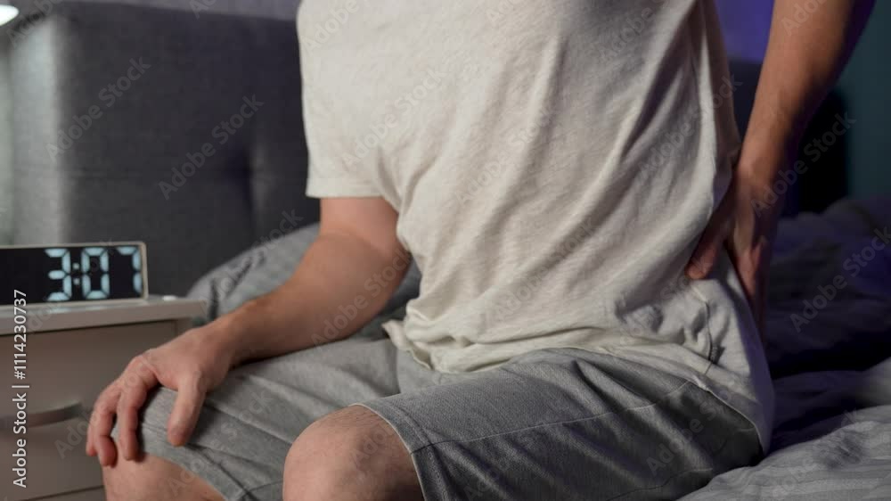 Man suffering from back pain, have a backache, health problems while sitting on bed in the bedroom at home, close-up. Man suffering from back pain, have a backache, health problems while sitting on bed in the bedroom at home, close-up.